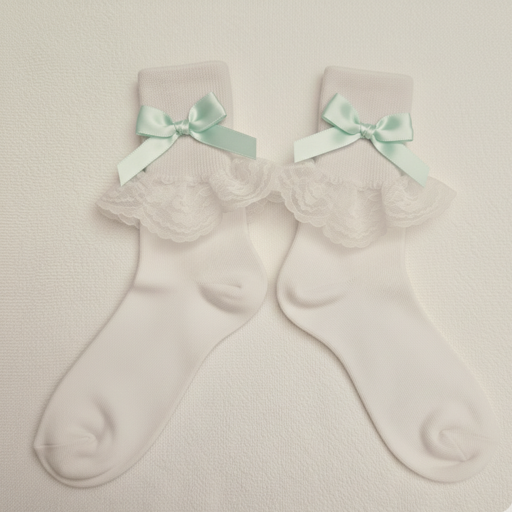 Pair of white socks with lace details and mint green bows on a beige background