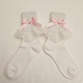 Pair of white socks with lace details and pink bows on a beige background