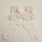 Pair of white socks with lace details and pink bows on a beige background