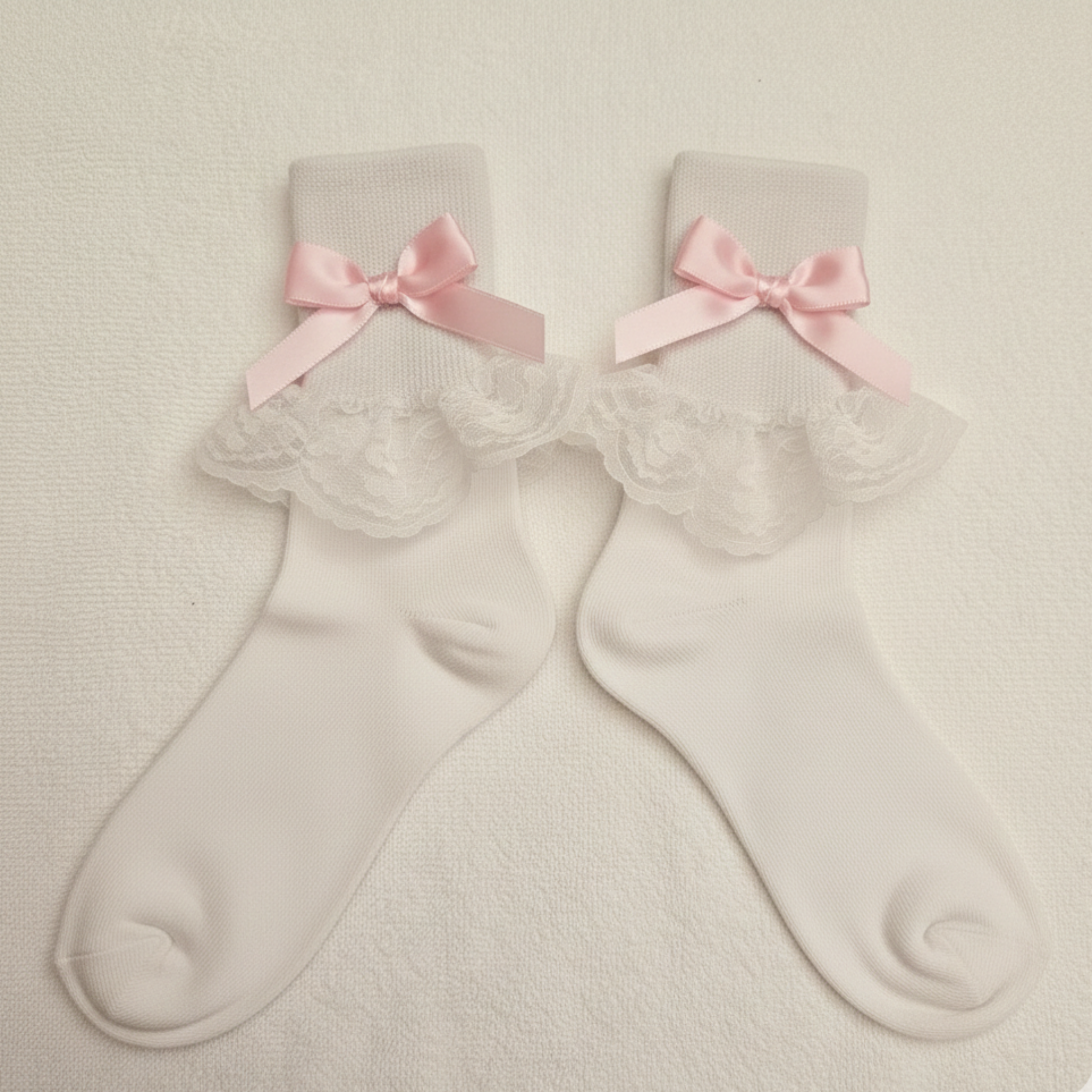 Pair of white socks with lace details and pink bows on a beige background