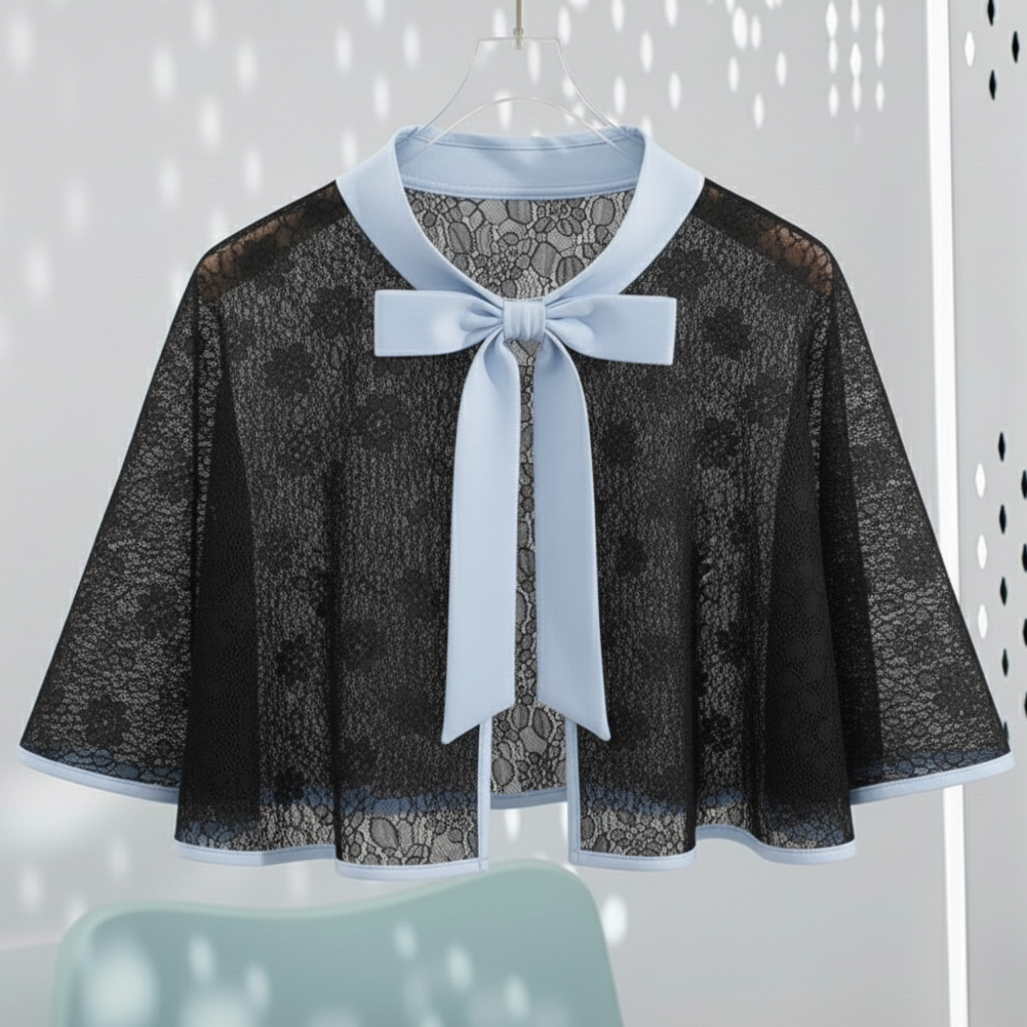 Black lace cape with a blue bow on a hanger against a light gray background