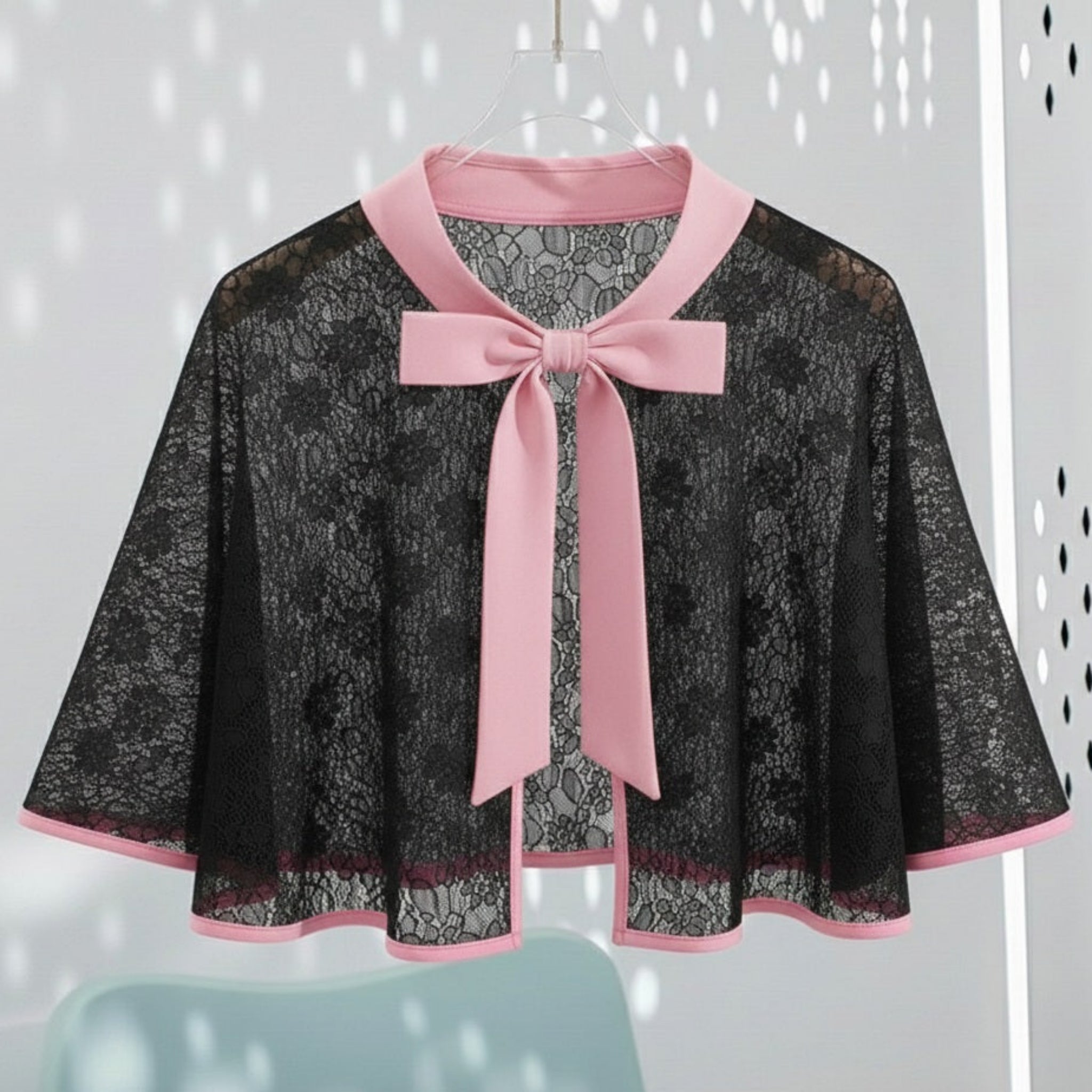 Black lace cape with pink trim and bow on a white background