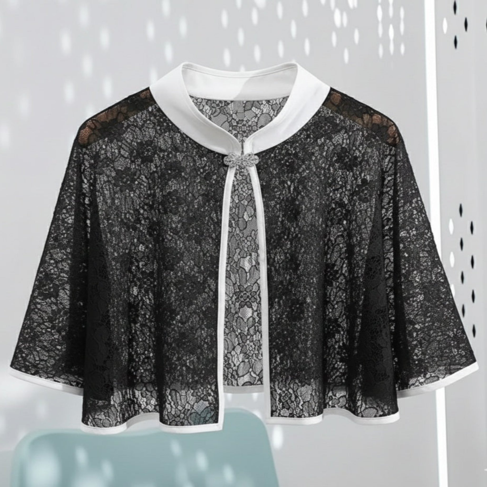 Black lace cape with white trim on a light gray background