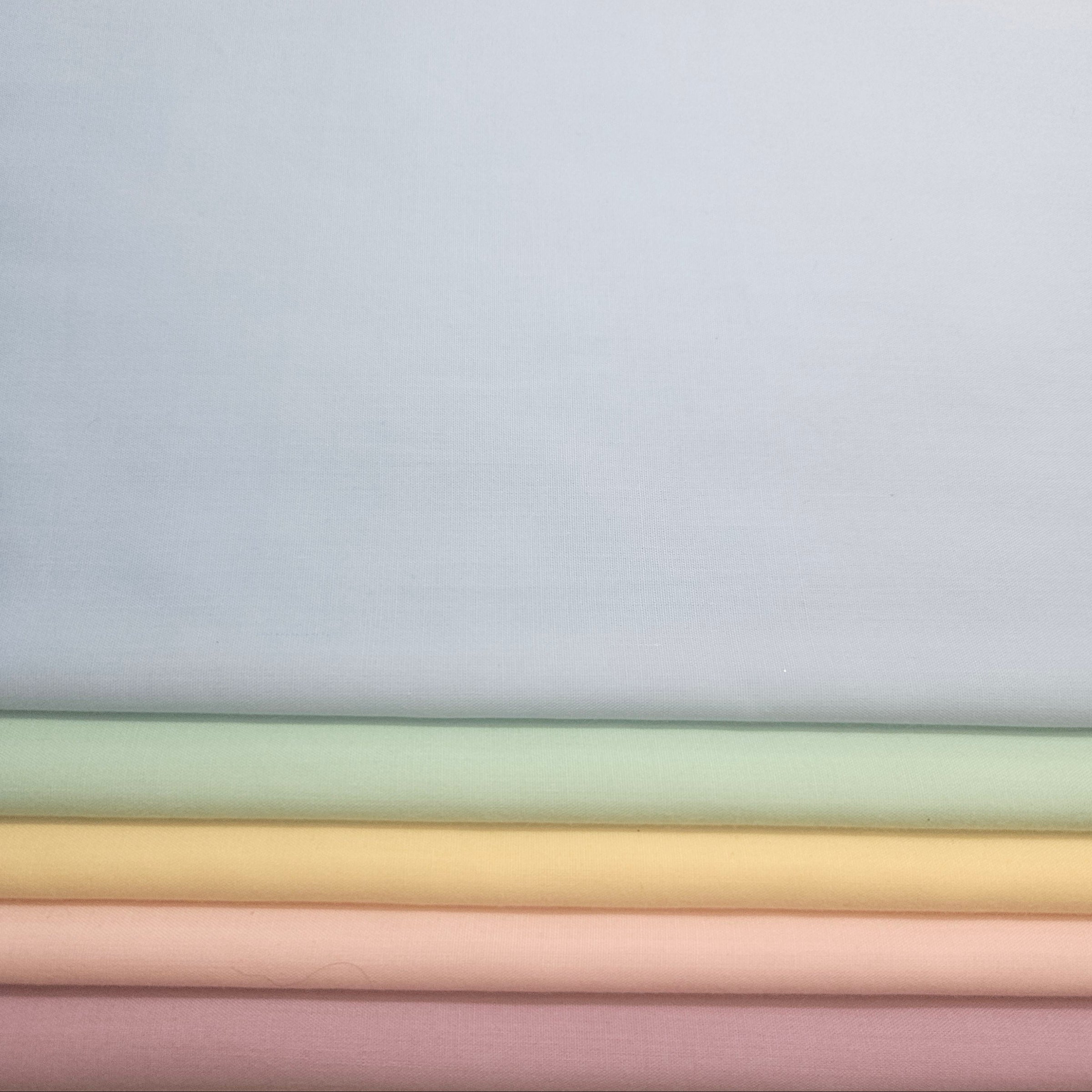Stack of pastel-colored fabrics on a light blue broadcloth background