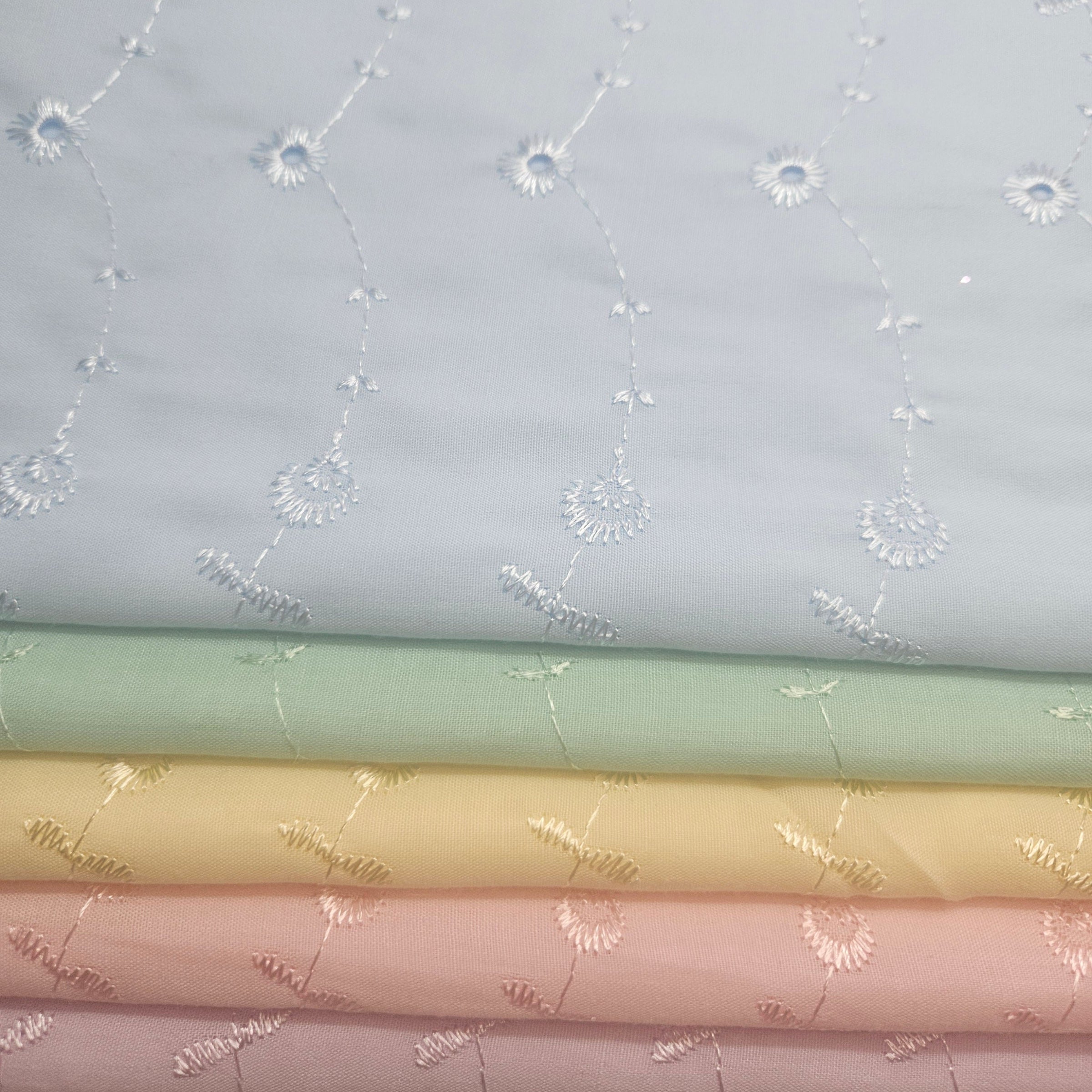 Stack of pastel-colored fabric swatches with decorative patterns and blue eyelet.