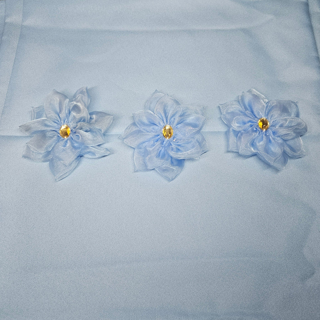 Three light blue flowers with gold centers on a light blue fabric background