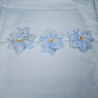 Three light blue flowers with gold centers on a light blue fabric background