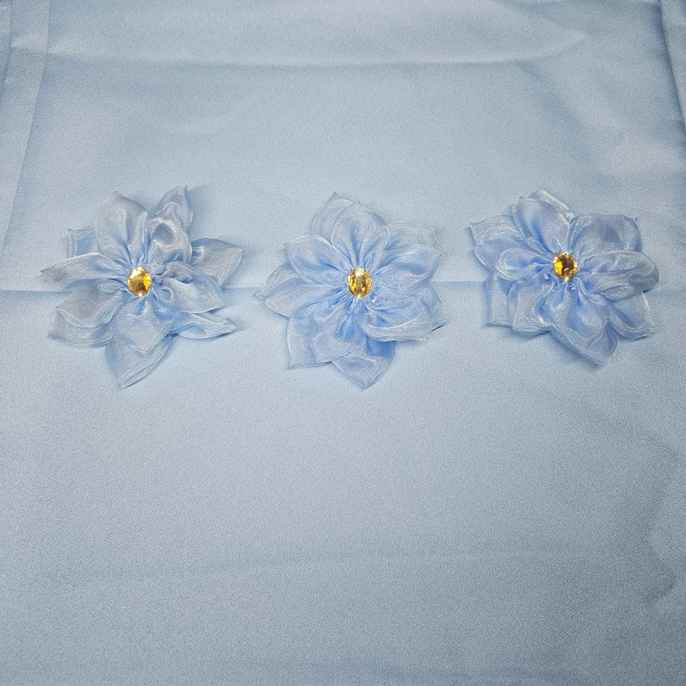 Three light blue flowers with gold centers on a light blue fabric background