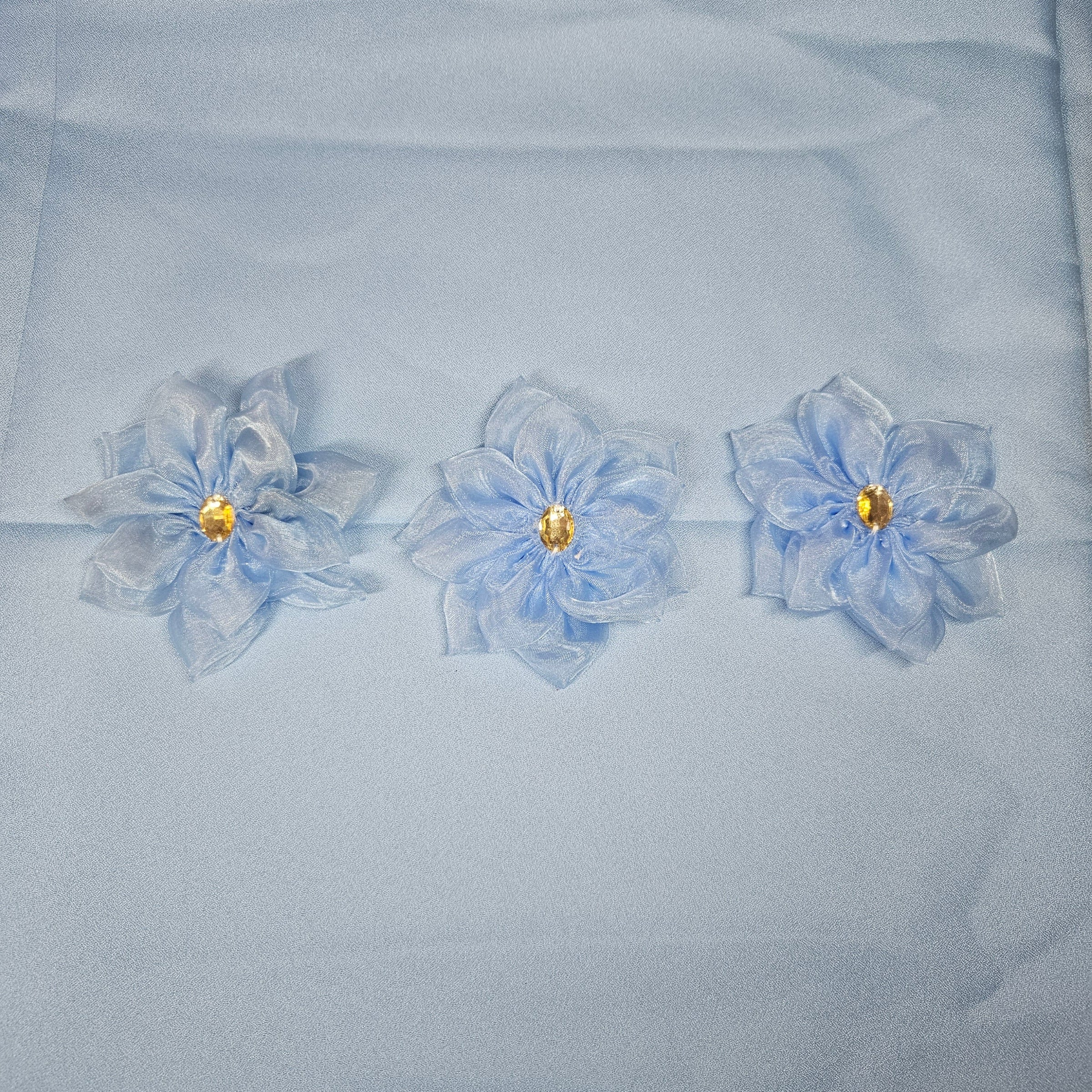 Three light blue flowers with gold centers on a light blue fabric background