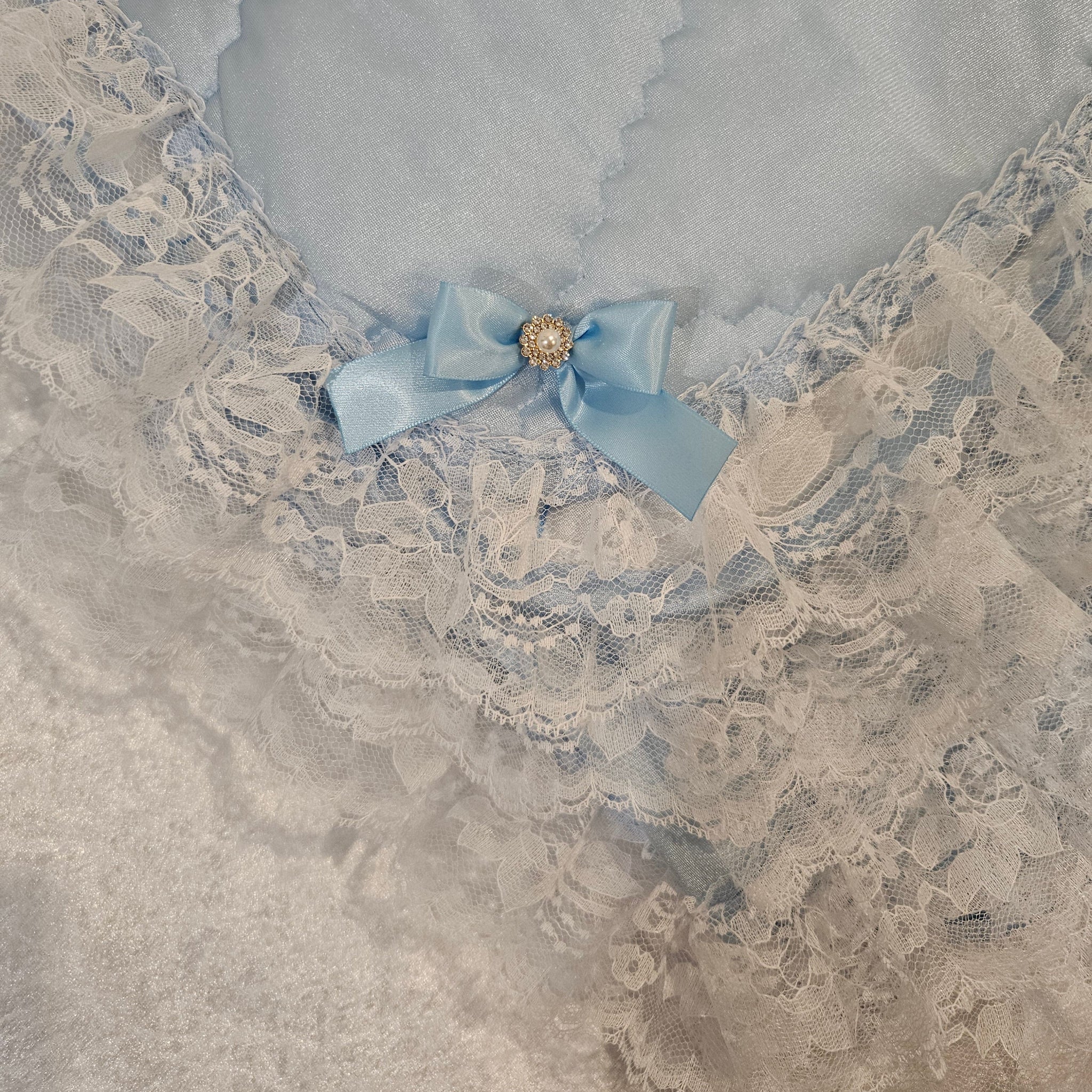Decorative blue snuggle blanket with lace trim and a blue bow on a textured surface
