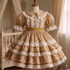 A vintage-style Lolita dress displayed on a wooden dress form mannequin. The dress features a brown and beige floral pattern with prominent white lace ruffles, a ruffled collar, and tiered skirt layers, set against a soft, warm bedroom background with a canopy bed and curtains.
