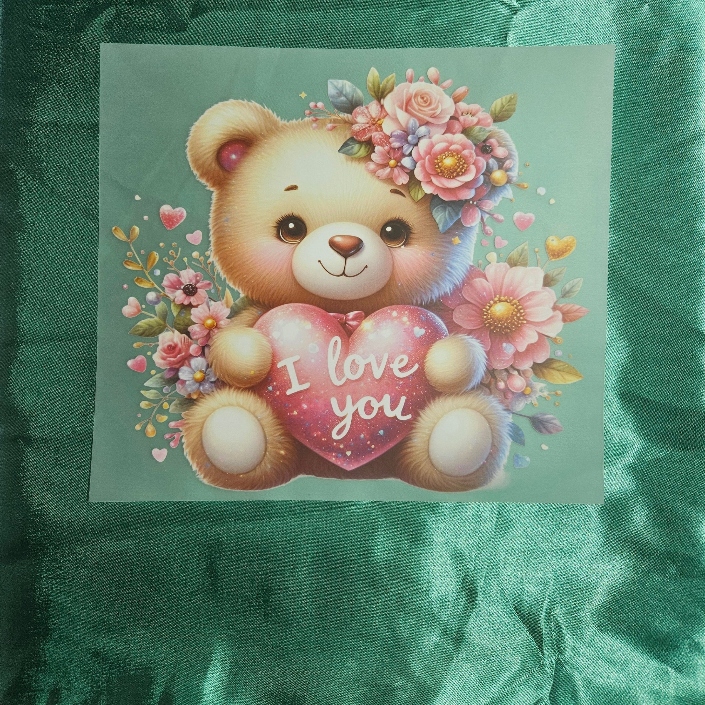 Cute teddy bear with floral crown and 'I love you' heart applique on a deep green satin fabric background