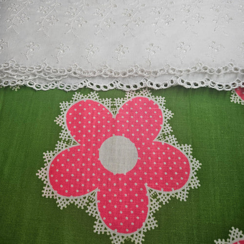 Pink flower with white polka dots on a green fabric background with lace trim.
