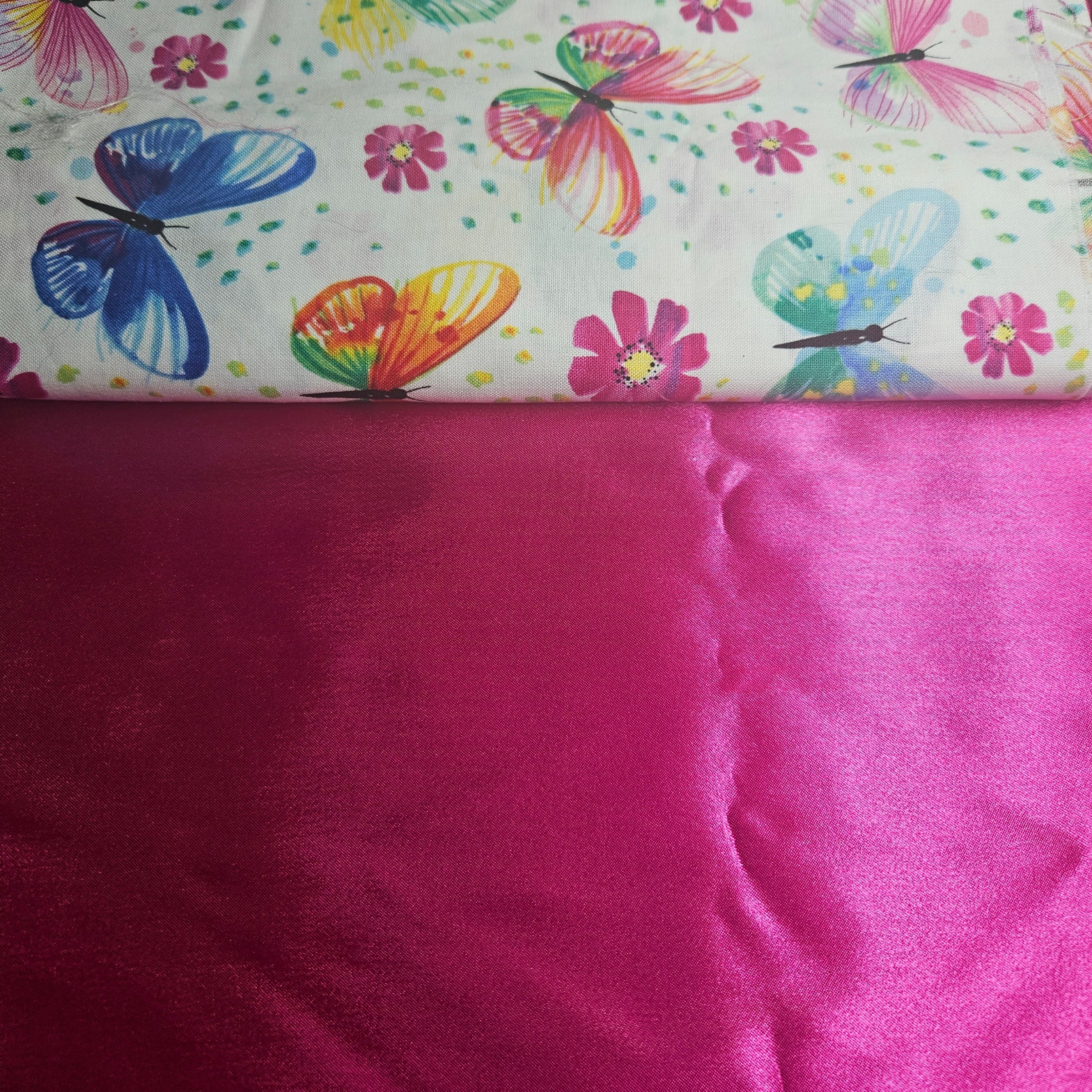 Fabric with colorful butterfly and flower pattern on top of a plain hot pink satin fabric.