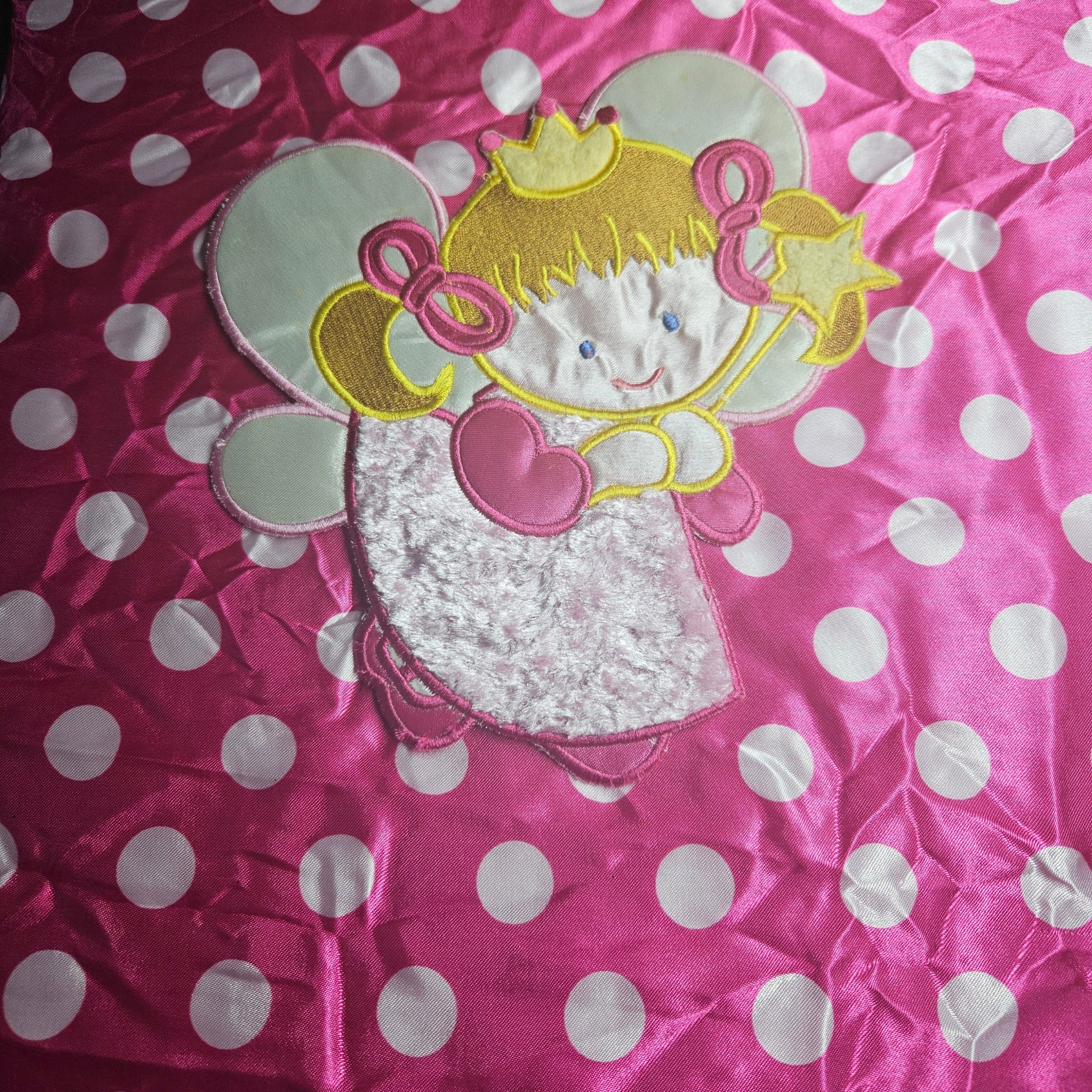 Pink fabric with white polka dots and a embroidered cartoon character applique.