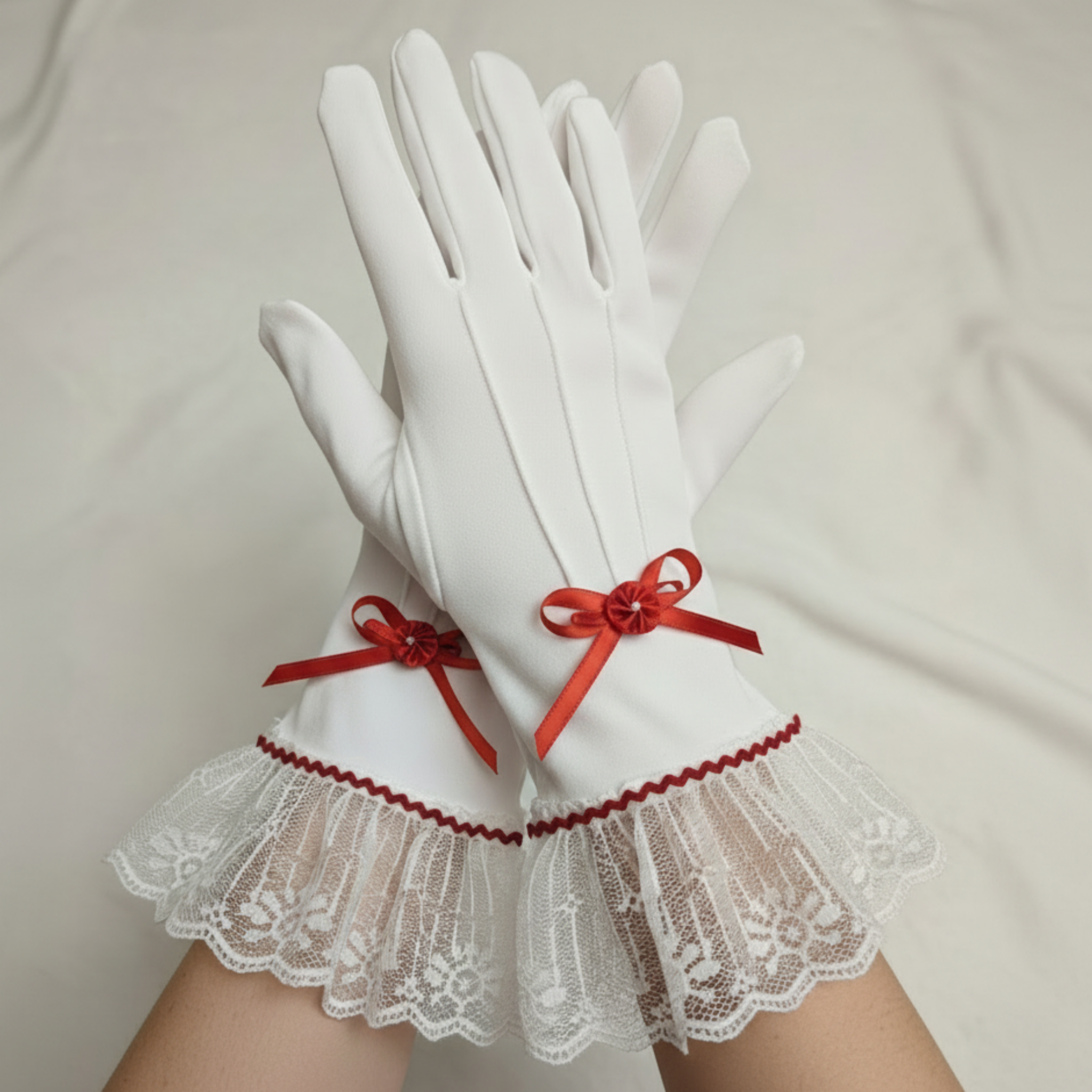 White gloves with lace cuffs and red ribbons on a white background
