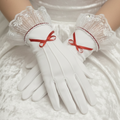 White gloves with red bows worn by a person in a white dress.
