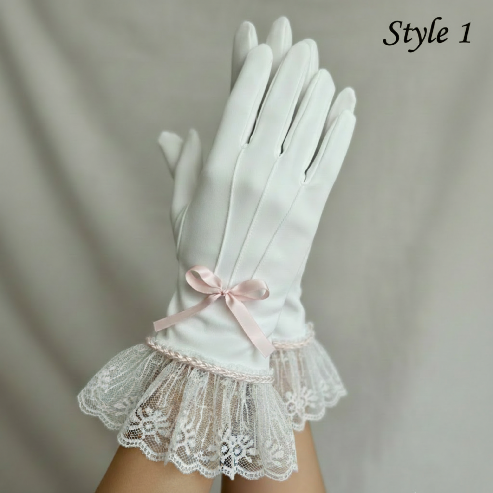 White gloves with lace cuffs and a pink bow on a neutral background
