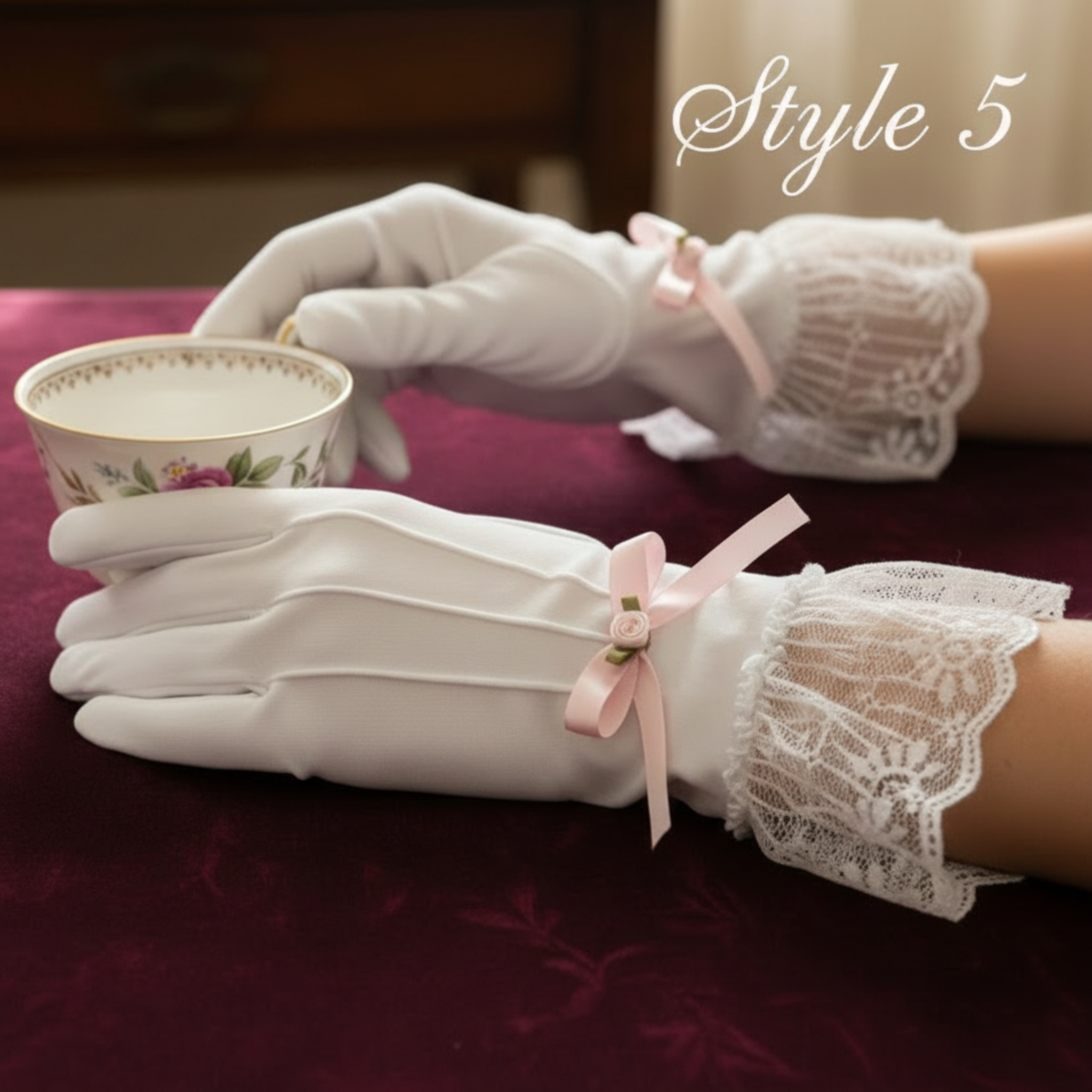 White lace gloves holding a small teacup on a maroon surface.