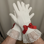 White gloves with lace cuffs and red satin bows on a neutral background