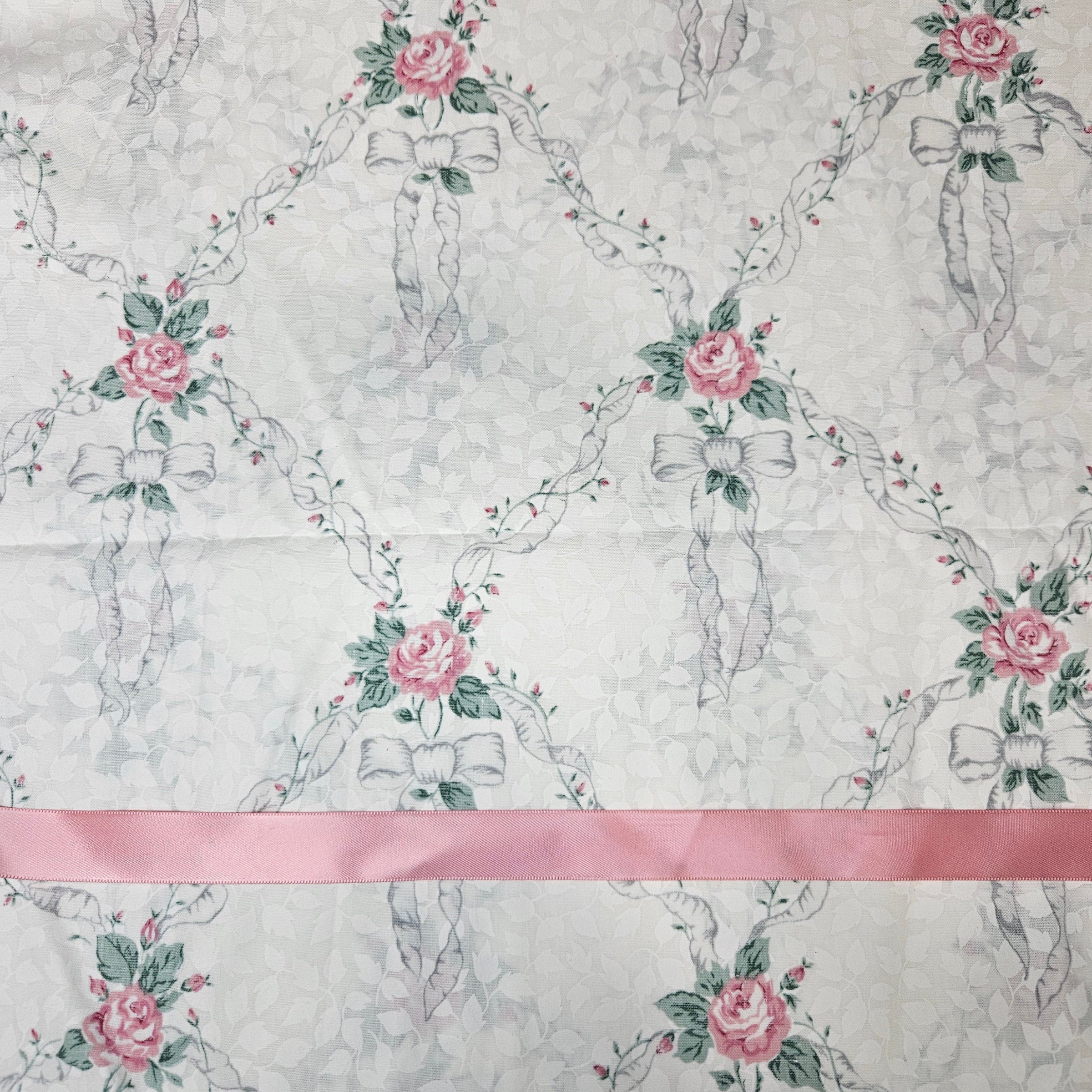 Patterned fabric with bow silhouettes, flowers, and ribbons on a light ivory background.