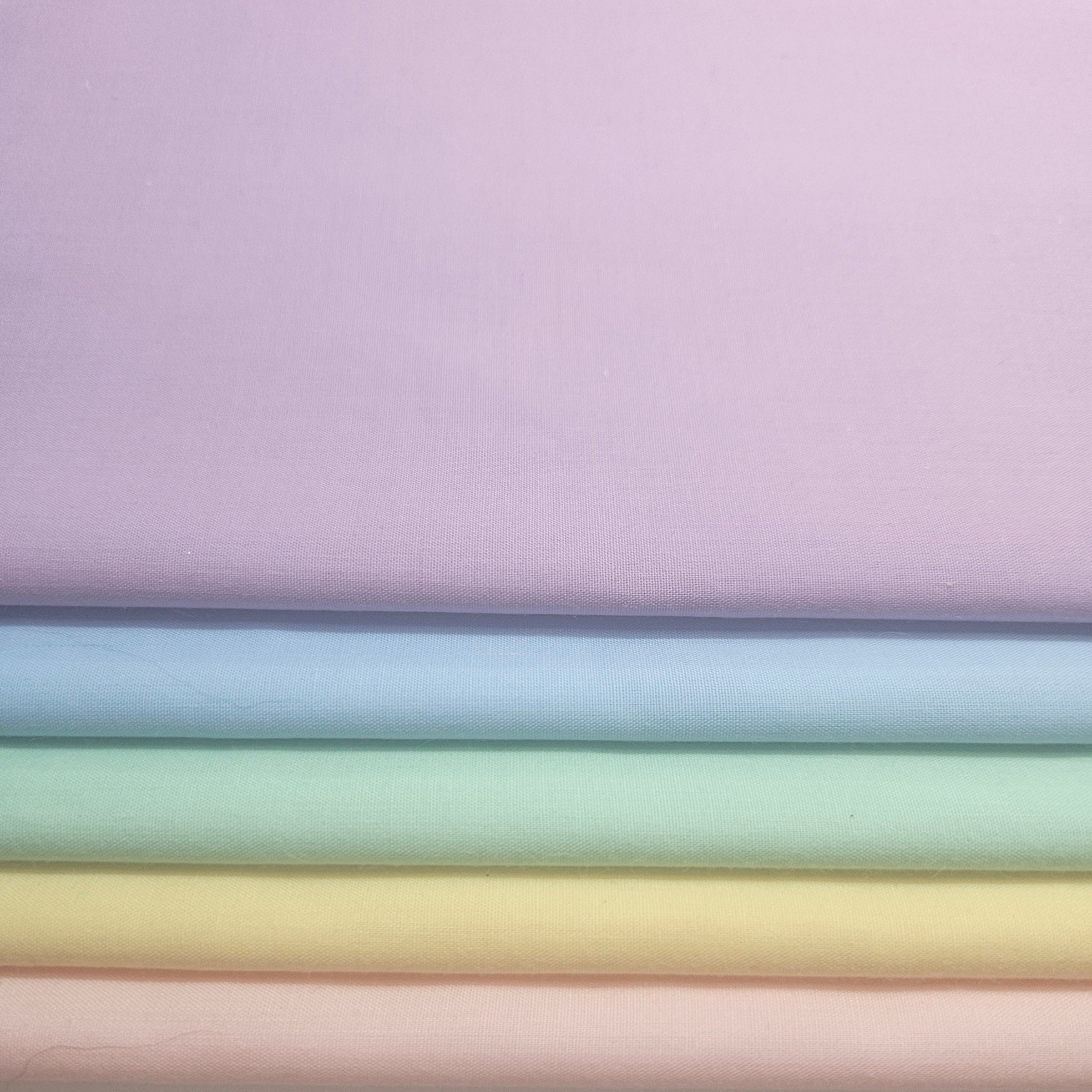 Stack of pastel colored fabrics with shades of pink, blue, green, lavender and yellow broadcloth