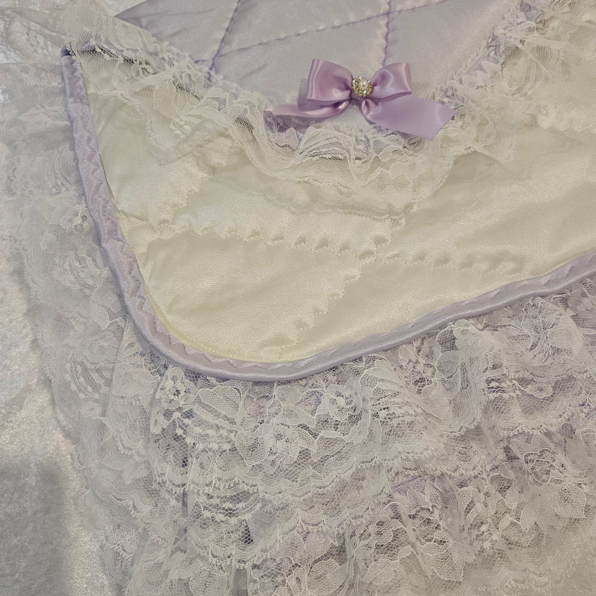 Close-up of a lavender snuggle blanket with lace detailing and a purple bow.