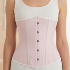 Woman wearing a light pink corset over a white top and pants on a neutral background