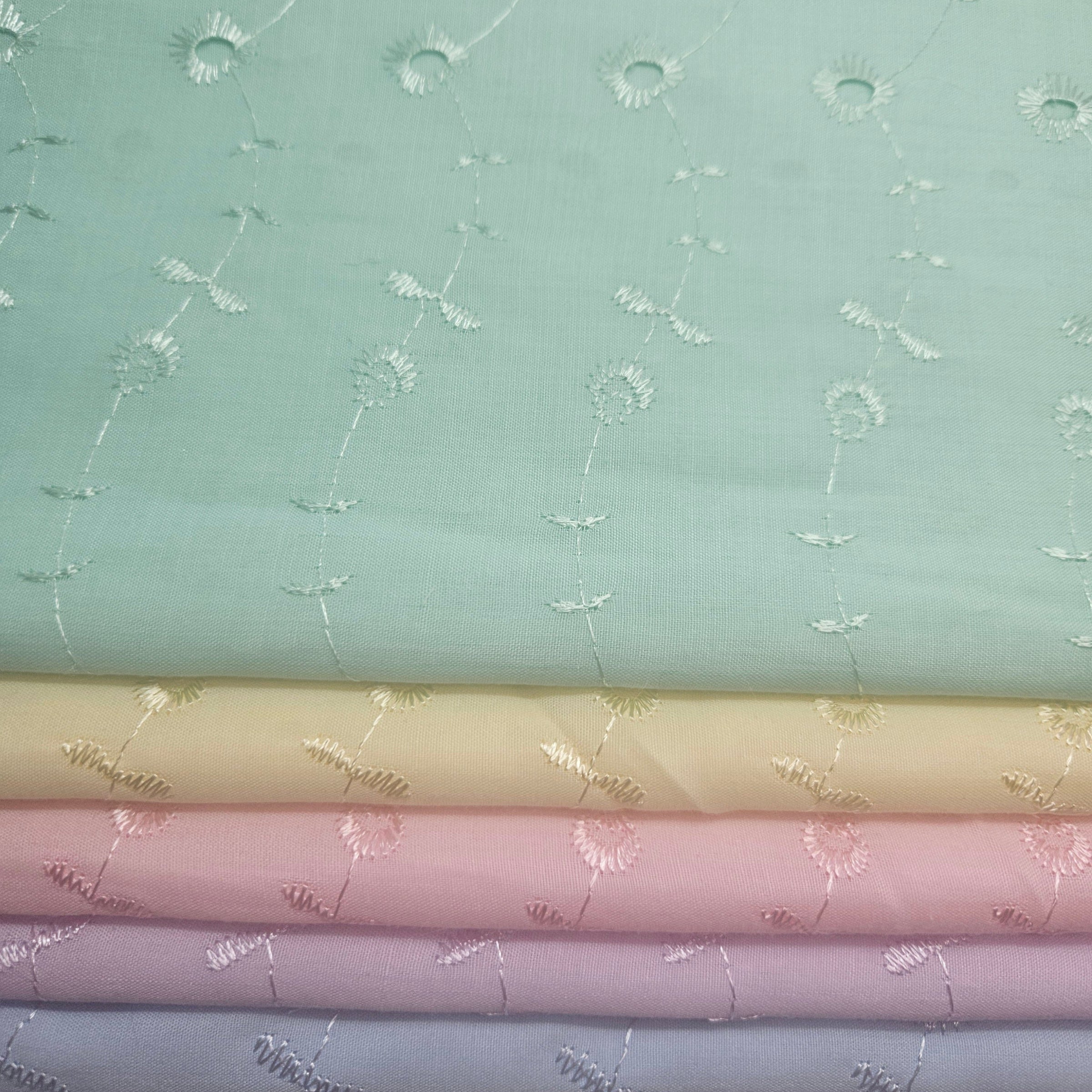 Stack of fabric swatches with floral patterns on a light green eyelet background
