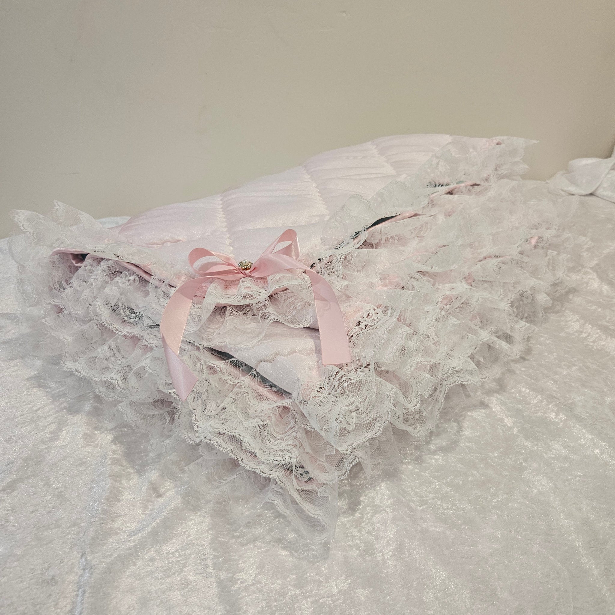 Close-up of a lace snuggle blanket with a pink ribbon on a plain background