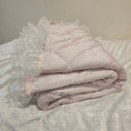 Light pink lace-trimmed snuggle blanket on a textured surface