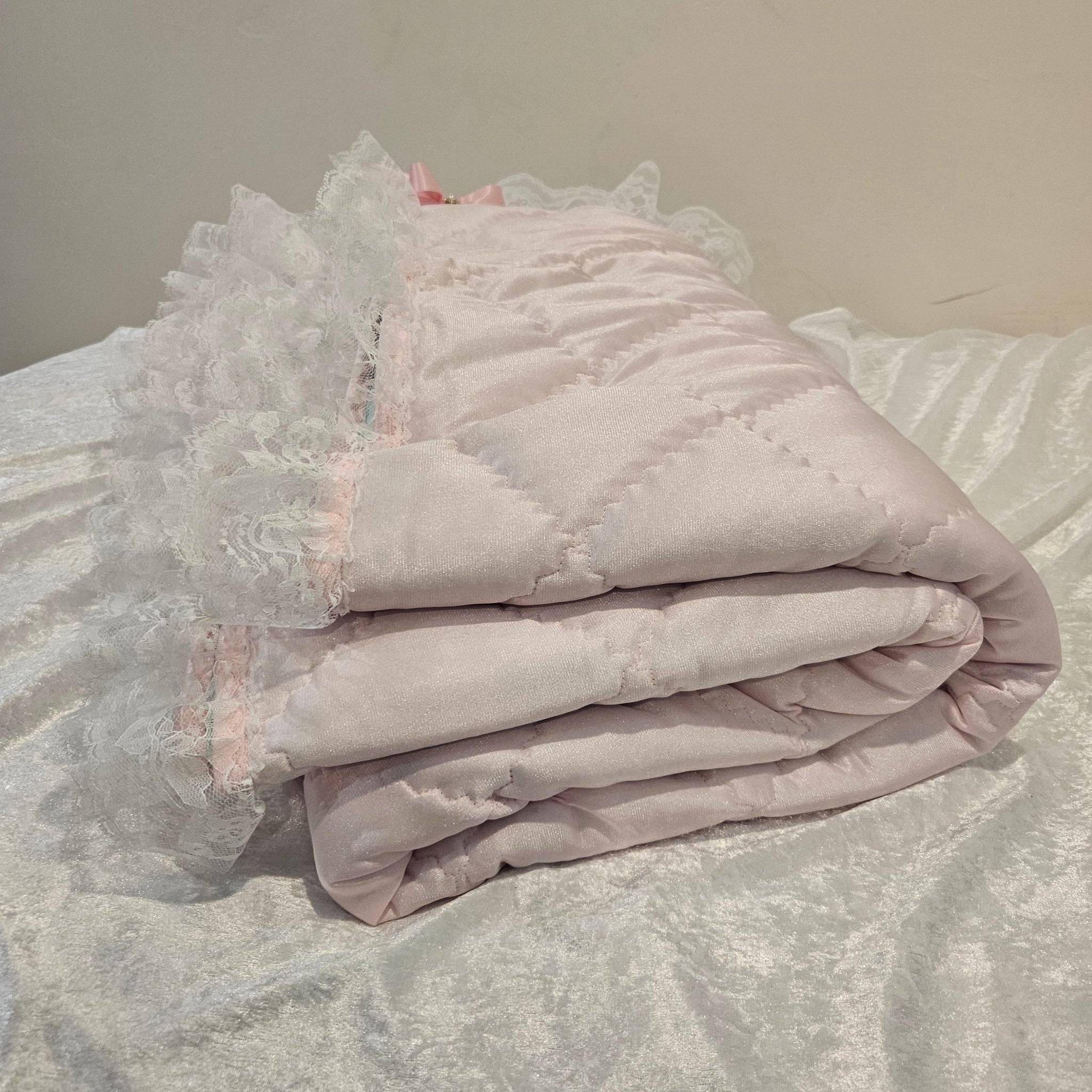 Light pink lace-trimmed snuggle blanket on a textured surface