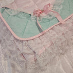 Light mint green snuggle blanket with lace trim and pink ribbon on a textured surface