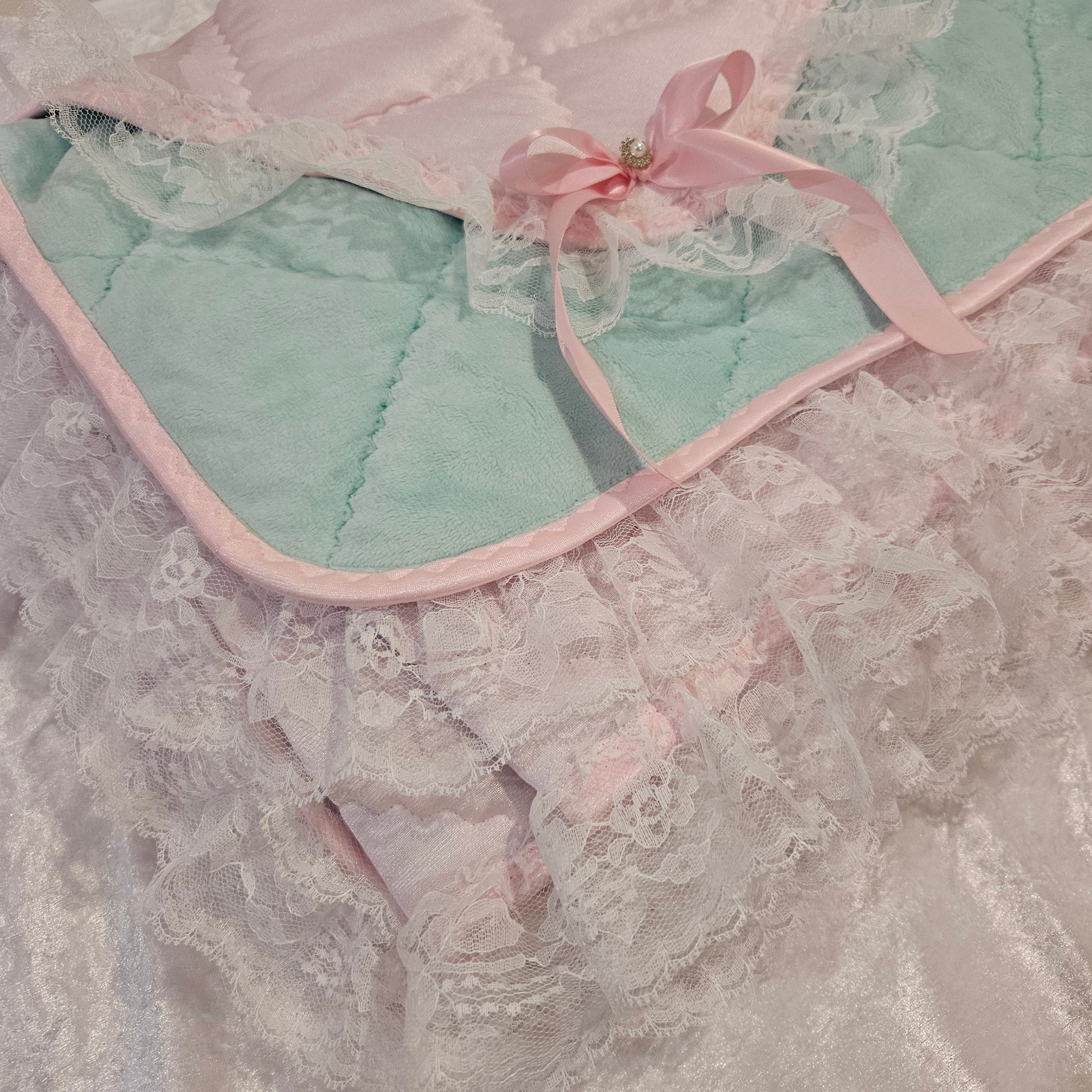 Light mint green snuggle blanket with lace trim and pink ribbon on a textured surface
