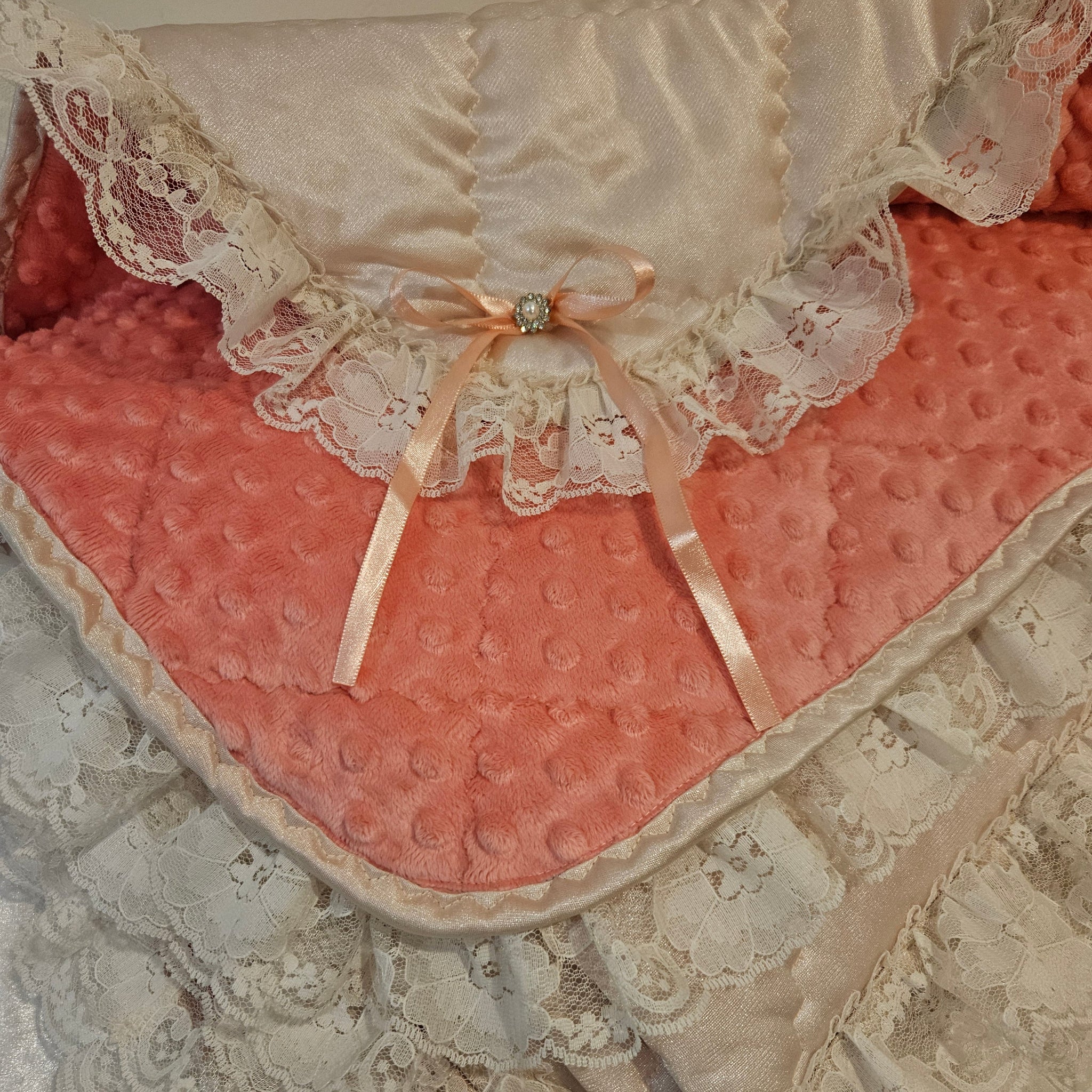 Peach snuggle blanket with lace trim and a bow and minky dots on a textured surface