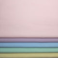 Stack of pastel fabric swatches in various colors on a light pink broadcloth background