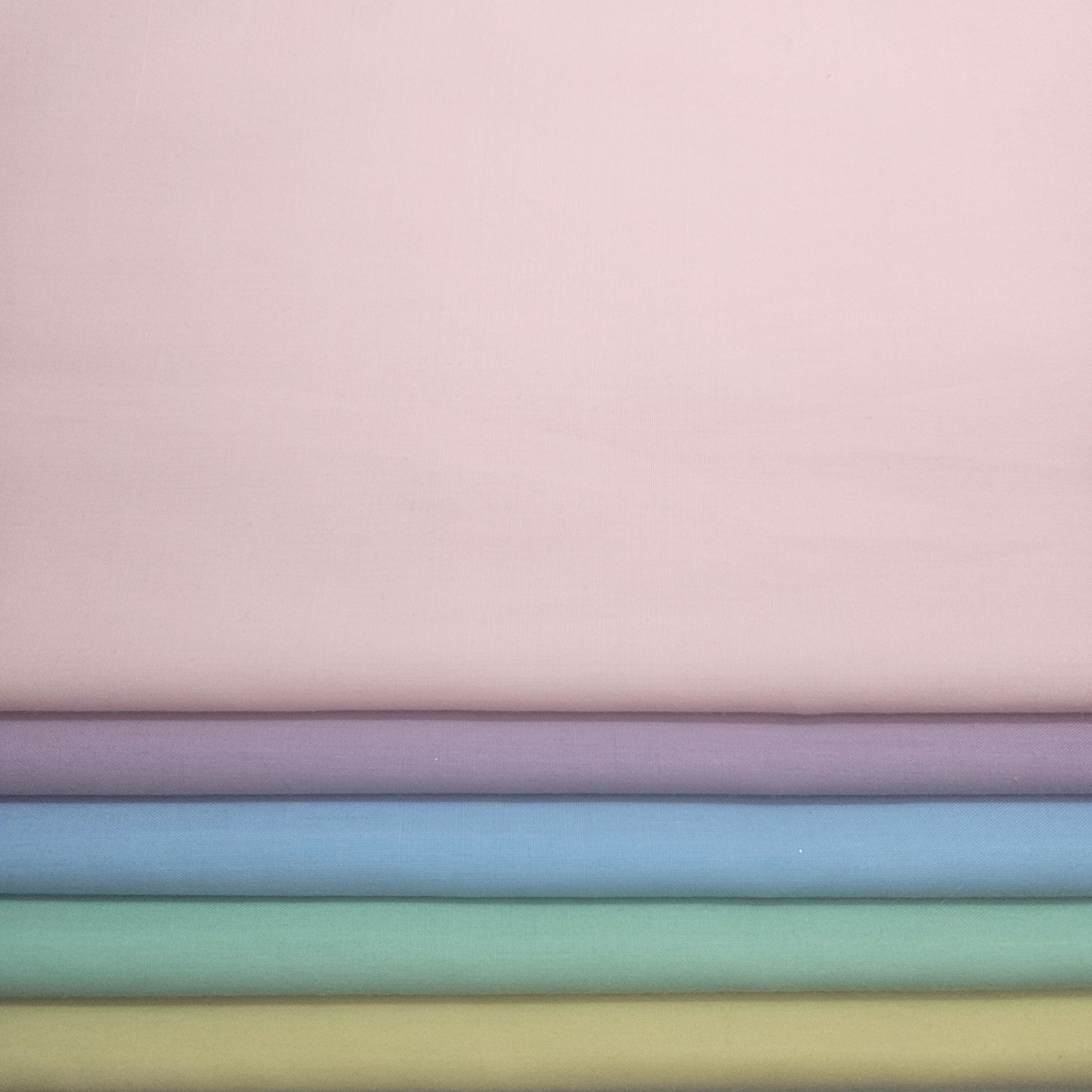 Stack of pastel fabric swatches in various colors on a light pink broadcloth background