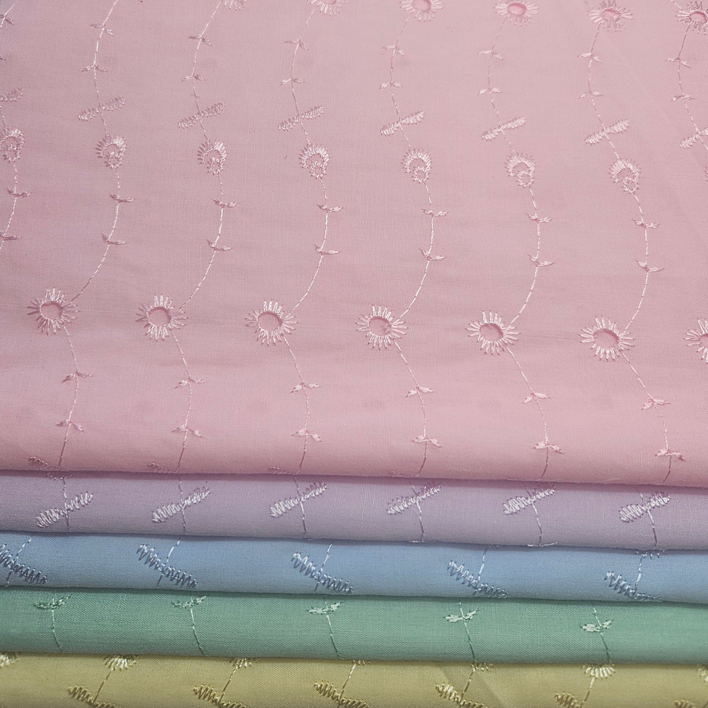 Stack of fabric swatches with floral patterns on a pink eyelet background