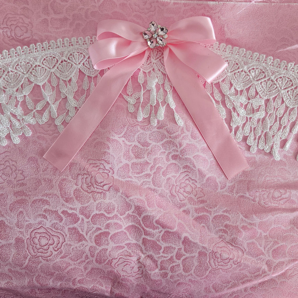 Pink floral rose damask fabric with Venise lace and  a bow with decorative brooch on a matching pink background