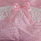 Pink floral rose damask fabric with Venise lace and  a bow with decorative brooch on a matching pink background
