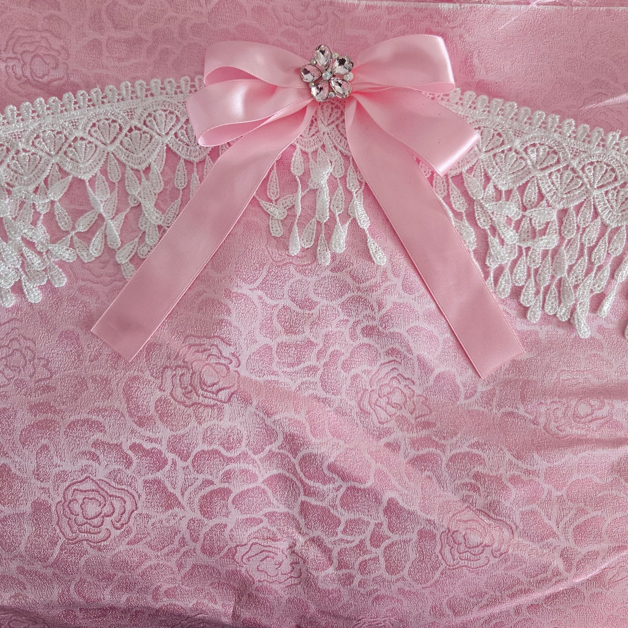 Pink floral rose damask fabric with Venise lace and  a bow with decorative brooch on a matching pink background