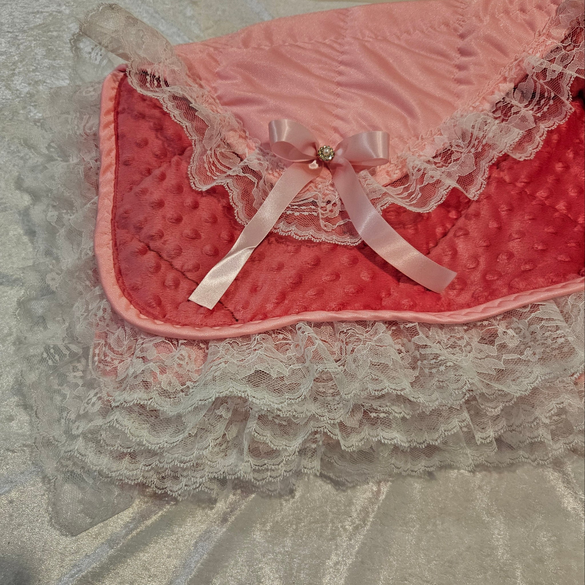 Close-up of a pink minky snuggle blanket with lace details on a neutral background