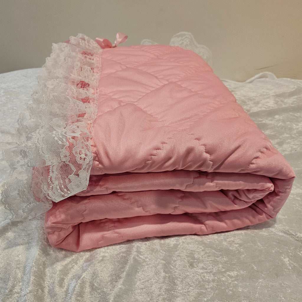 Pink minky snuggle quilt with lace trim draped over a textured surface