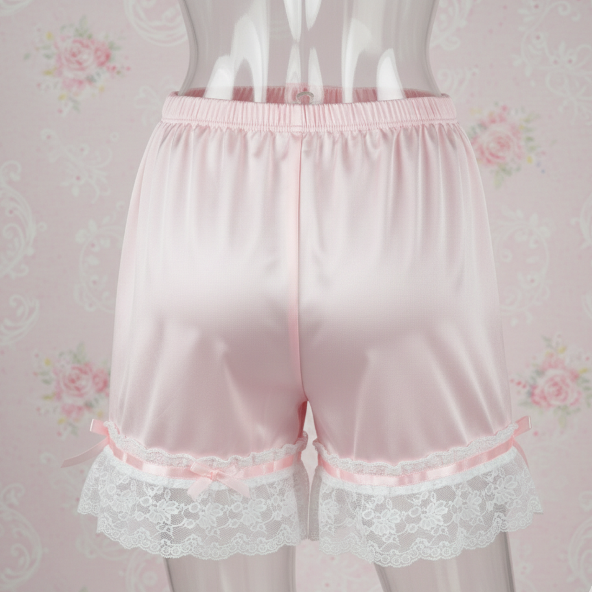 Pink satin sleep shorts with lace trim on a floral background