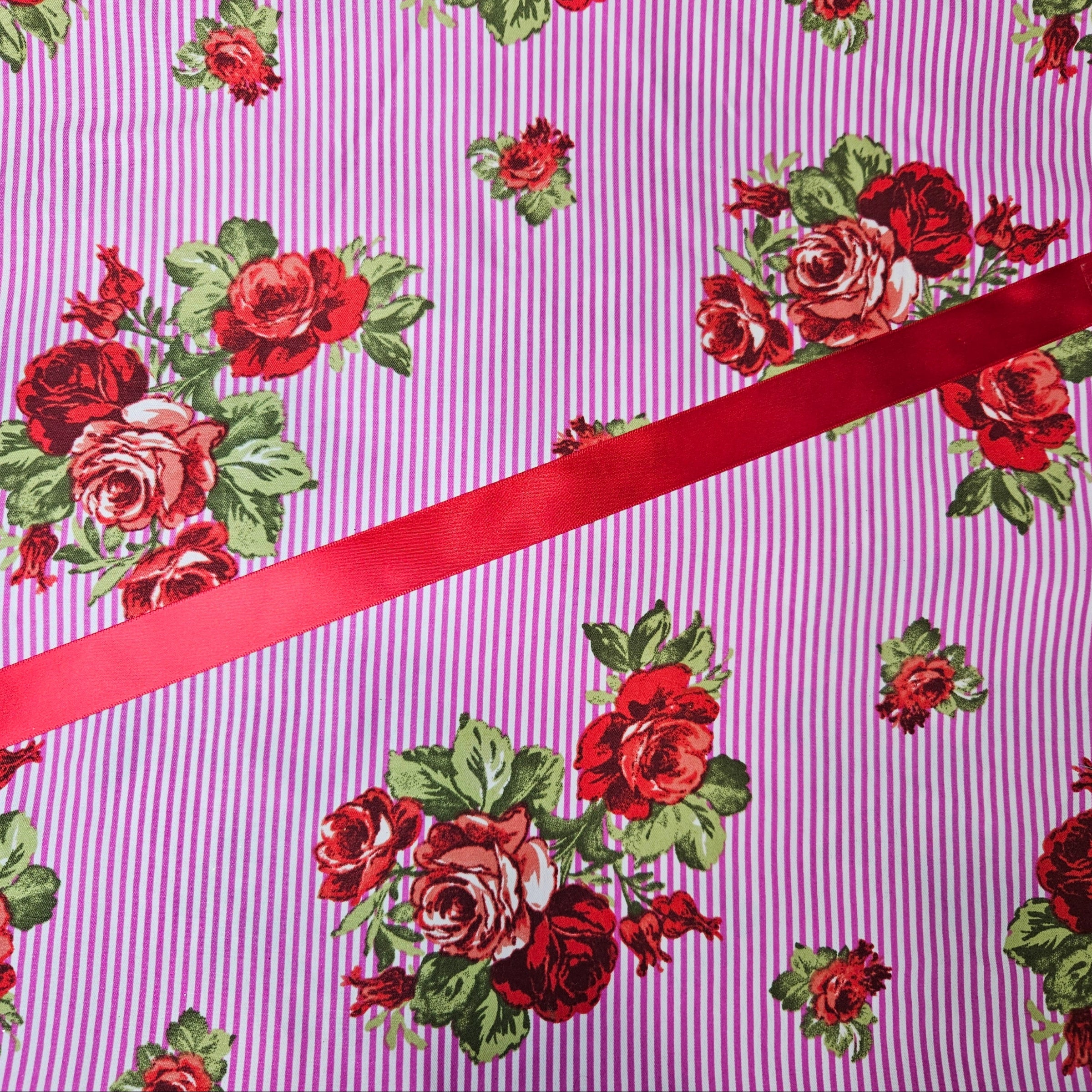 Fabric with red floral pattern and a red ribbon on a pink striped background