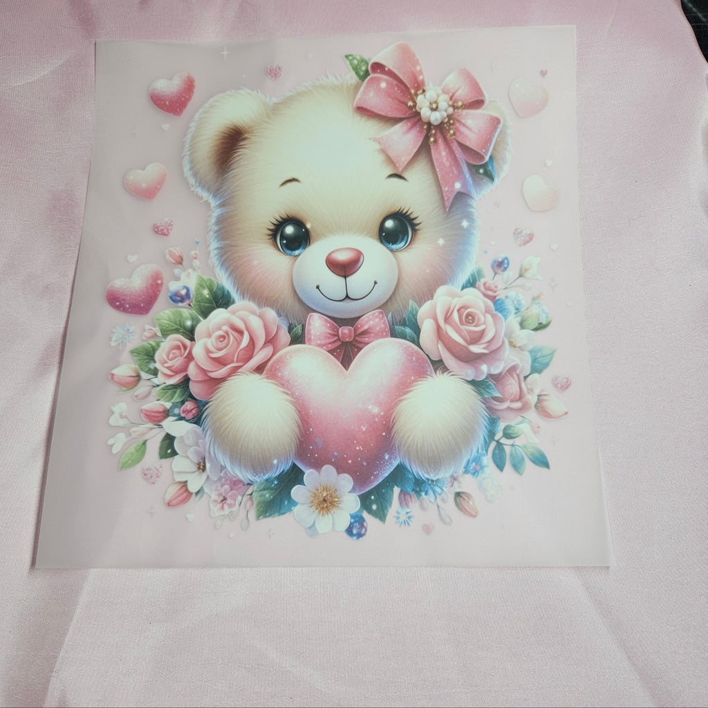 Cartoon teddy bear applique with a pink bow and heart surrounded by flowers on a light pink taffeta background