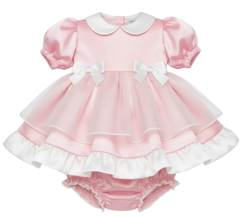 Pink satin baby dress with white ruffles and bow details on a white background