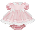 Pink satin baby dress with white ruffles and bow details on a white background