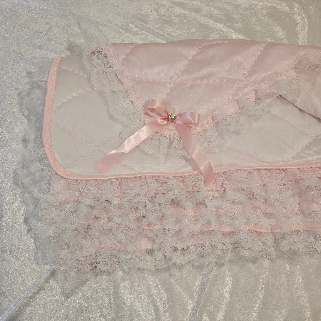 Light-colored Pink Snuggle quilt with trim on a textured surface