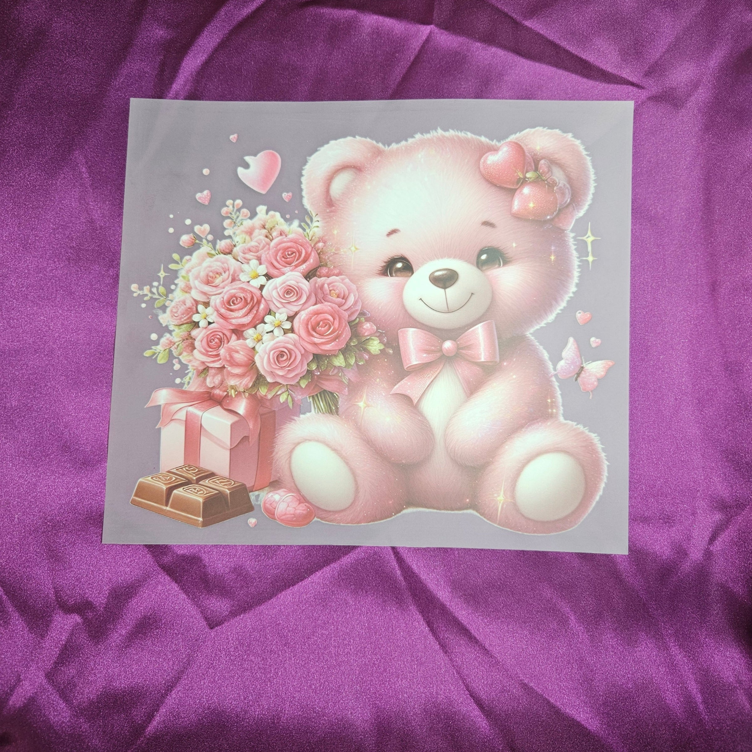 Pink teddy bear applique with flowers and a gift on a purple satin fabric background